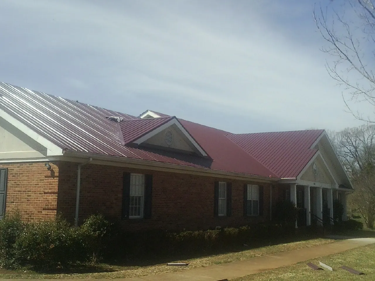 Red metal roof with gabled entries on a long brick building, from a Hail Damage Roof Repair job in East Longmeadow