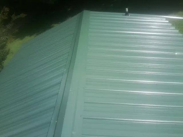 New green metal panels meeting at the ridge of a roof — Flat Roof Repair work by our crew in East Longmeadow