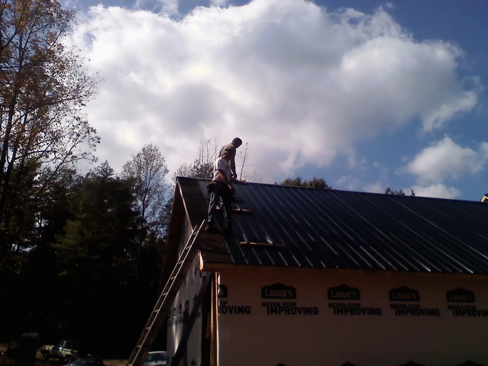 Roofer fastening dark metal panels high against a cloudy sky, from a Roof Inspection job in East Longmeadow