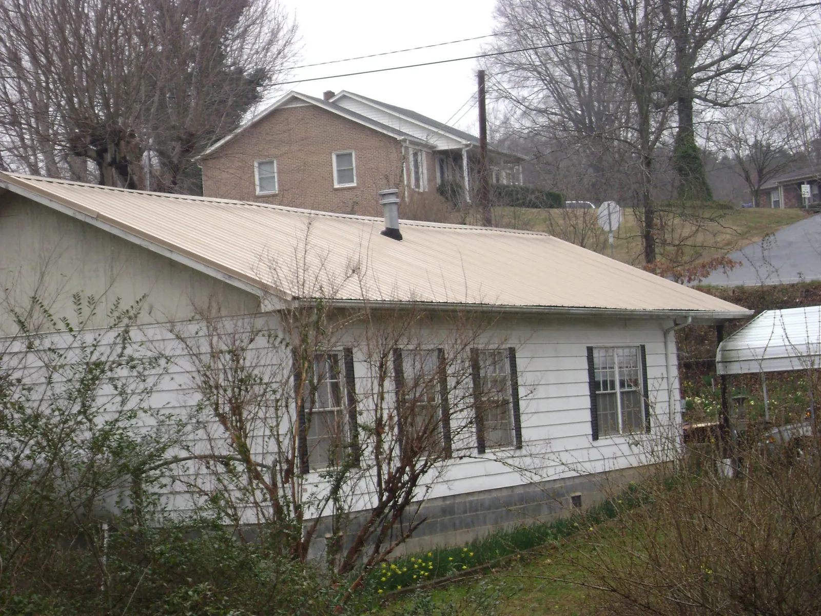 Tan metal roof on a white sided house set into a hillside — Commercial Roofing by Roofing Brothers in East Longmeadow